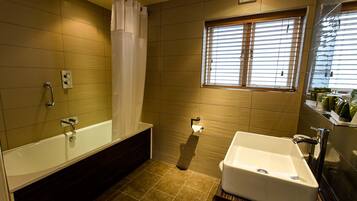 Un baño con bañera, lavamanos y ventana con persianas.