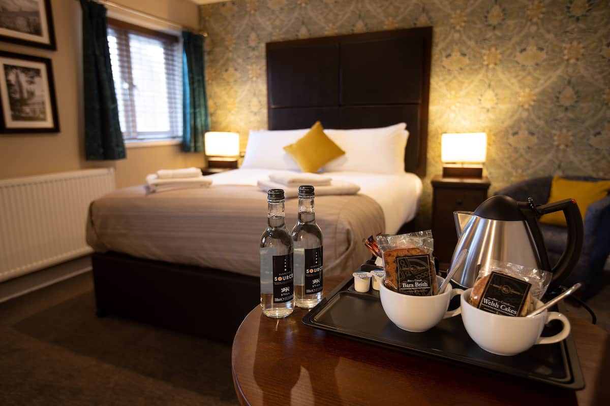 A hotel room with a neatly made bed, two bedside lamps, a tray with toiletries, and a view of the room's patterned wallpaper.