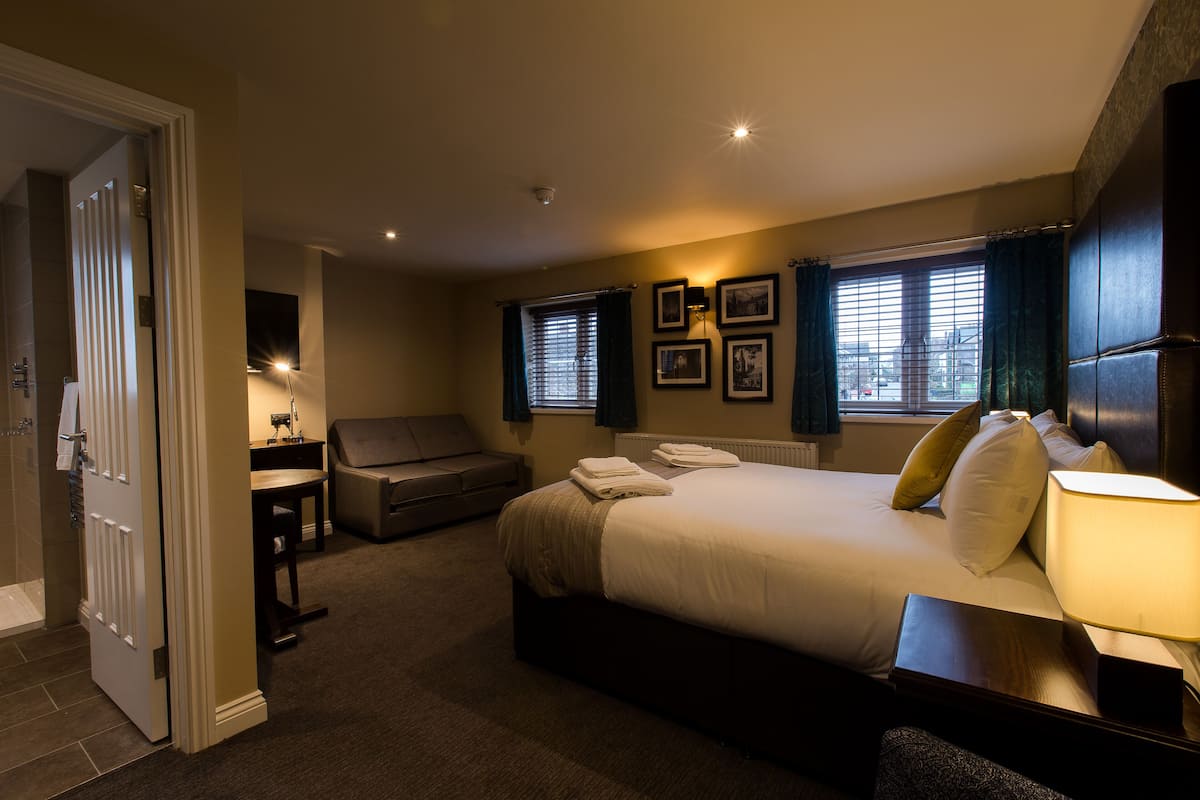 A hotel room with a bed, bedside table, lamp, and a view of the city through the window.