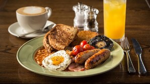A plate of breakfast with eggs, sausages, beans, tomatoes, and toast, accompanied by a cup of coffee and a glass of orange juice. - The Maltsters Arms (Cardiff)