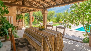An outdoor patio with a table covered by a striped tablecloth, surrounded by potted plants and a view of a swimming pool. - VILLA FRONTERA - Villa with private pool and views to the mountains in Soller Free WiFi (S��ller)