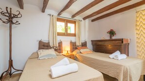 A room with two beds, a wooden coat rack, a window with curtains, a nightstand with a lamp, and a dresser with a vase of flowers. - VILLA FRONTERA - Villa with private pool and views to the mountains in Soller Free WiFi (S��ller)