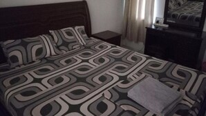 Une chambre à coucher avec une couvre-lit à motifs, une table de chevet, un miroir et une fenêtre avec des rideaux.