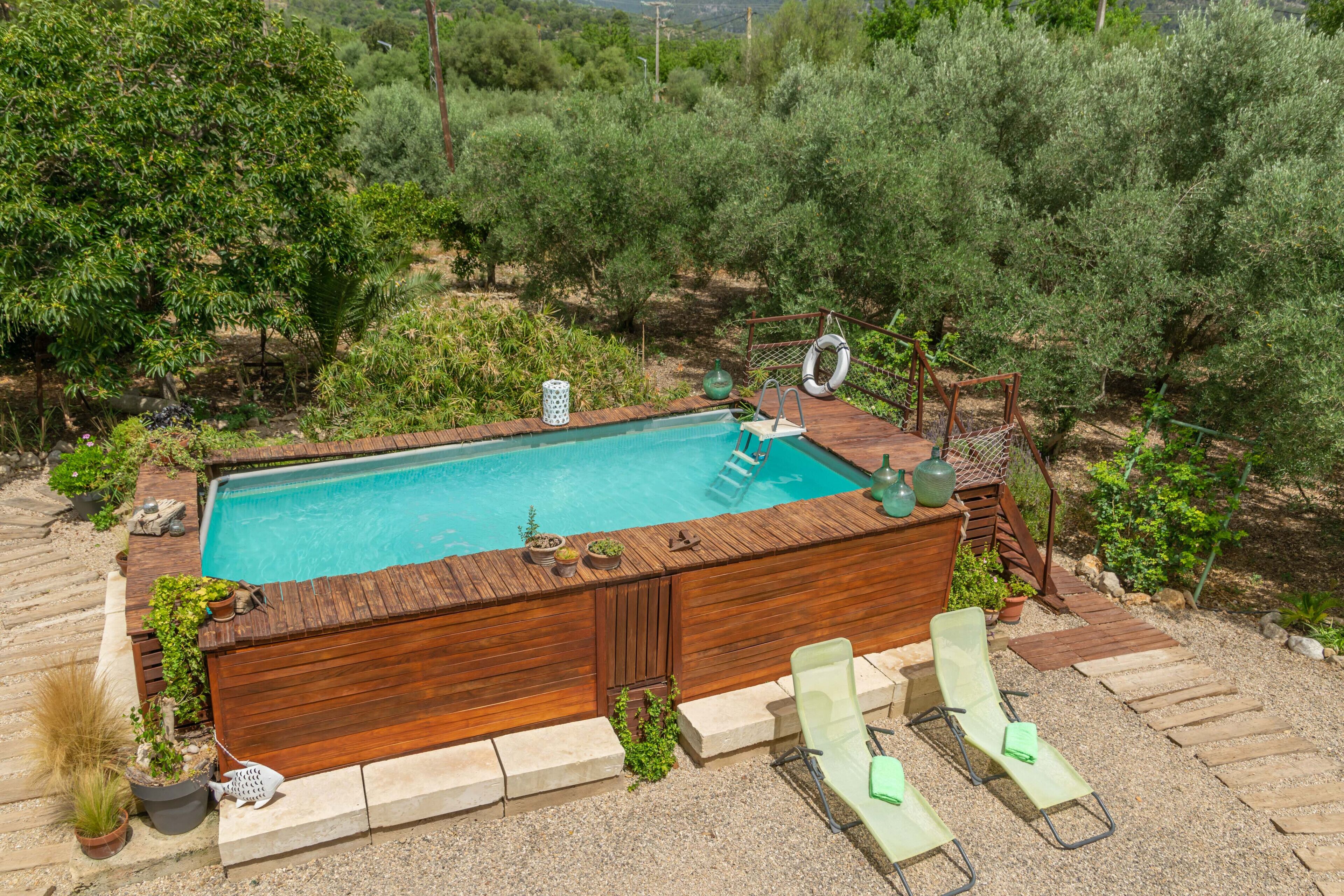 A rectangular wooden hot tub with a ladder and a small table, surrounded by a gravel deck and two green lounge chairs.