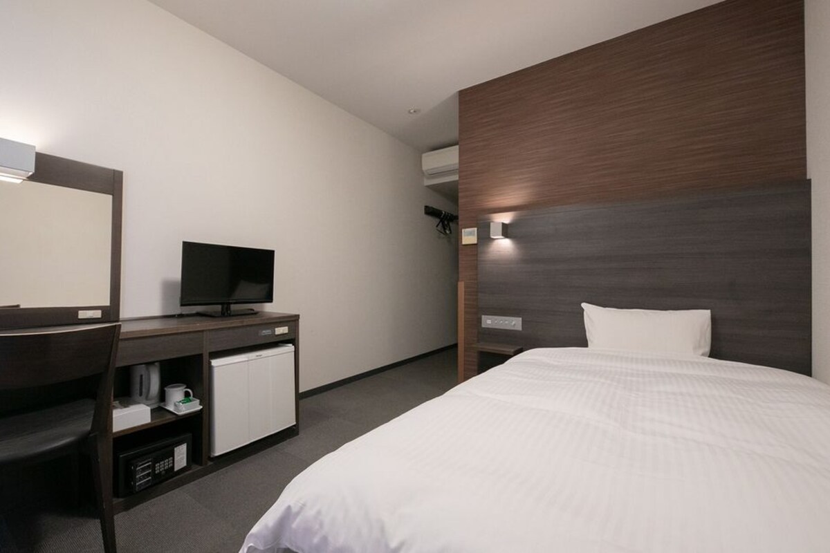 A hotel room with a bed, a desk with a computer, a chair, and a mirror.