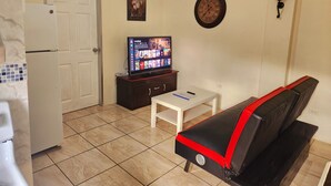 A compact living space with a kitchenette, a television, a sofa, and a small table. - Stewart Suite Apt -Trincity, Airport, Full Apt (Trincity)