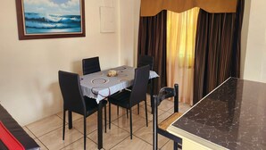A dining area with a table set for four, chairs, a painting on the wall, and a curtain. - Stewart Suite Apt -Trincity, Airport, Full Apt (Trincity)