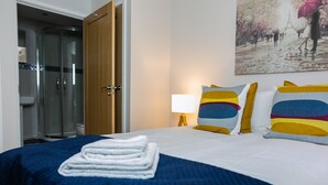 A hotel room with a bed, a bedside lamp, a painting, and a shower area. - The Pinnacle by Jim Paul Apartments (Reading)