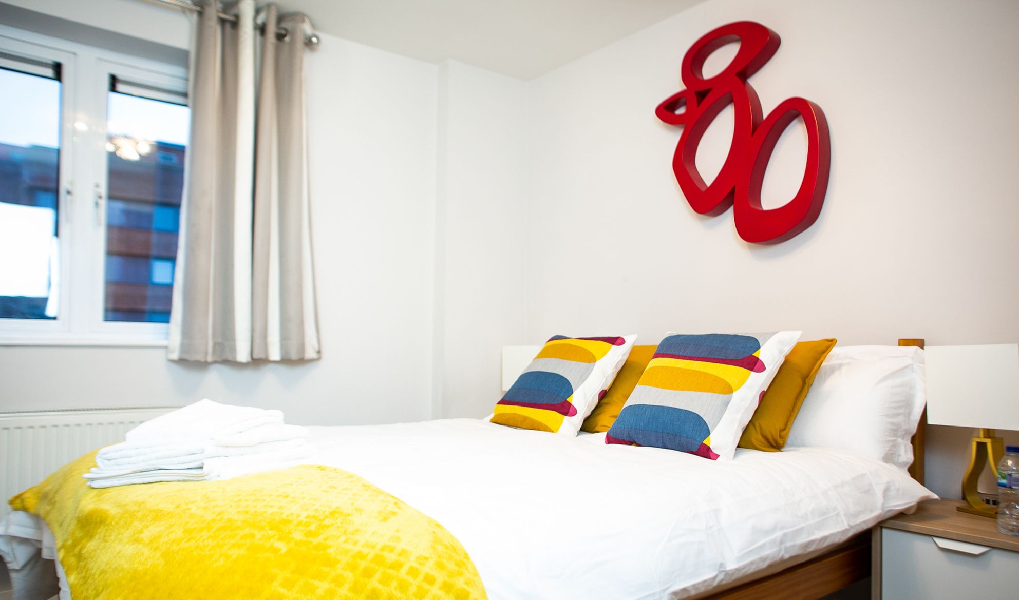 A hotel room with a bed, a large window with curtains, and a wall-mounted number '80'.