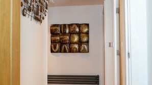 A hallway with wooden flooring, a radiator, and a wall-mounted abstract art piece. - The Pinnacle by Jim Paul Apartments (Reading)