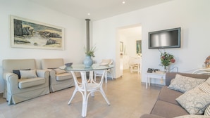 Een woonkamer met een bank, stoelen, een glazen tafel, een schilderij en een televisie.