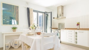 Een moderne keuken met witte kastjes, een eettafel gedekt voor twee personen en een groot raam met gordijnen.
