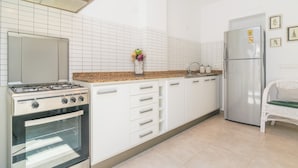 Een moderne keuken met witte kasten, een gasfornuis, een oven, een koelkast en een rieten stoel.