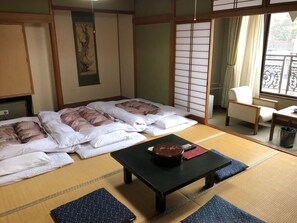 A traditional Japanese room with tatami flooring, two beds with pillows, a black table with a bowl, and a sliding door. - Yumura Onsen Totoya (Shinonsen)