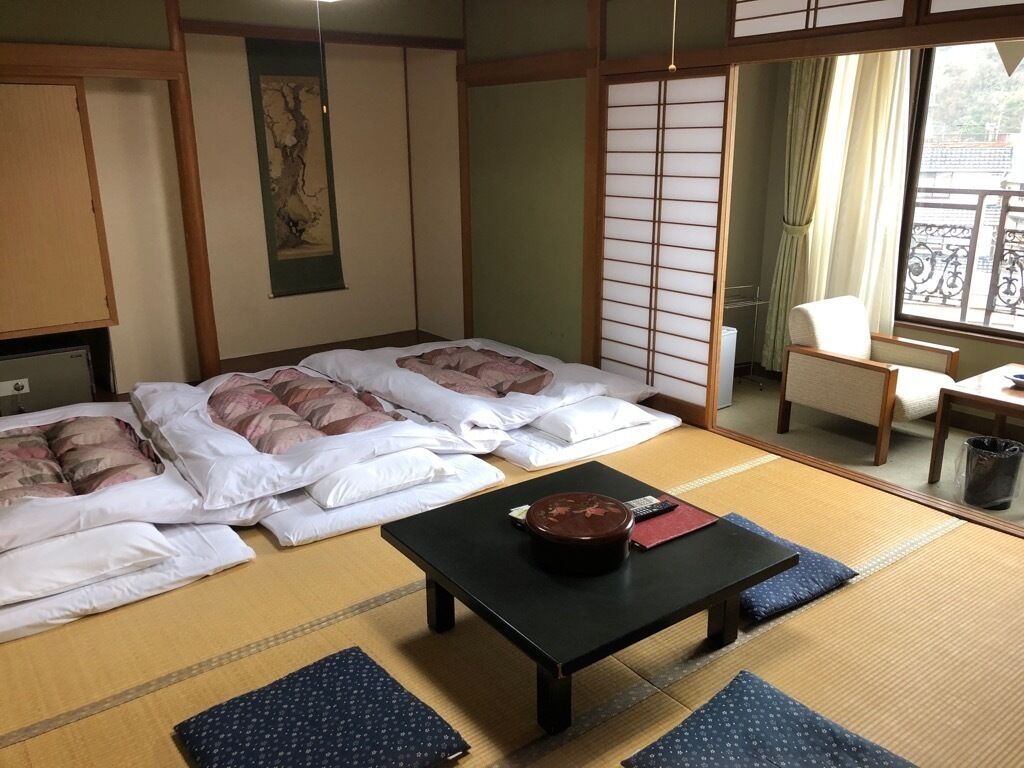 Una habitación japonesa tradicional con suelo de tatami, dos camas con almohadas, una mesa negra con un cuenco y una puerta corredera.