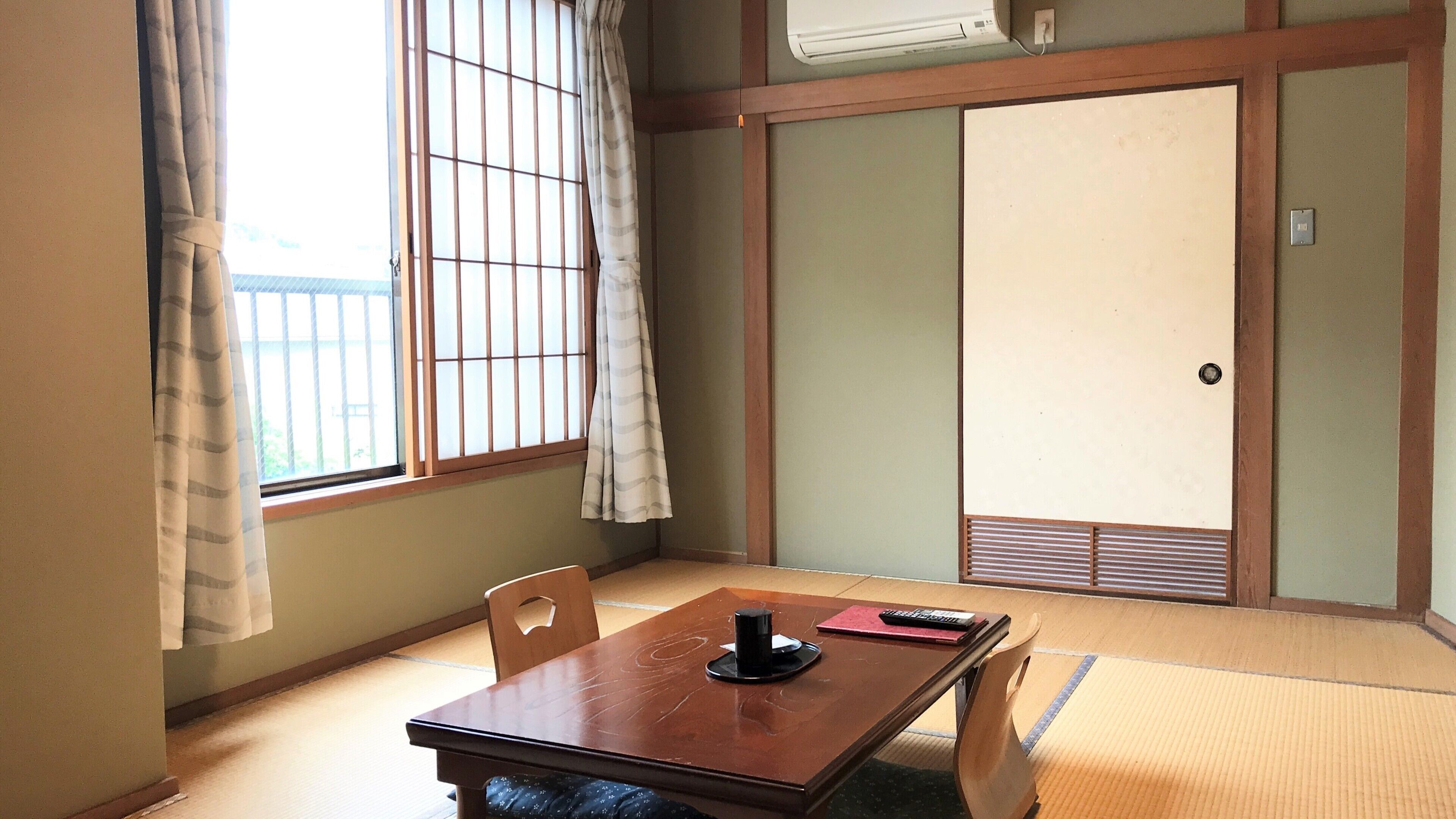 Una habitación japonesa tradicional con suelo de tatami, una puerta corredera y una mesa con un objeto negro encima.