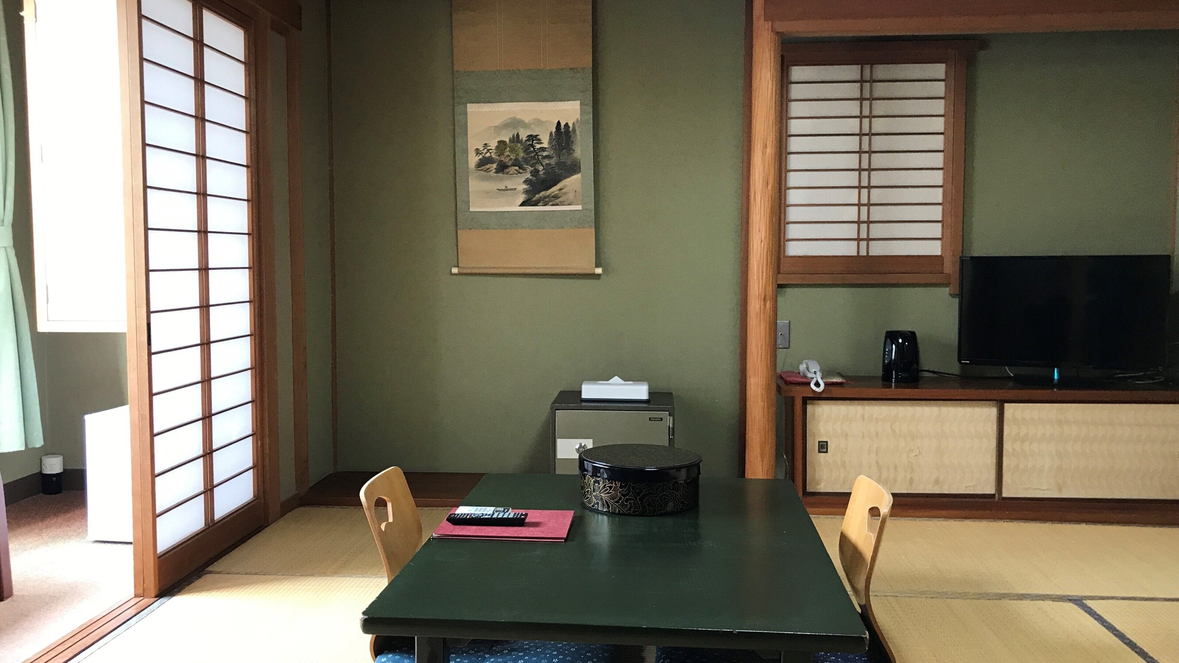 Una habitación japonesa tradicional con suelo de tatami, una mesa baja, un televisor y un cuadro en la pared.