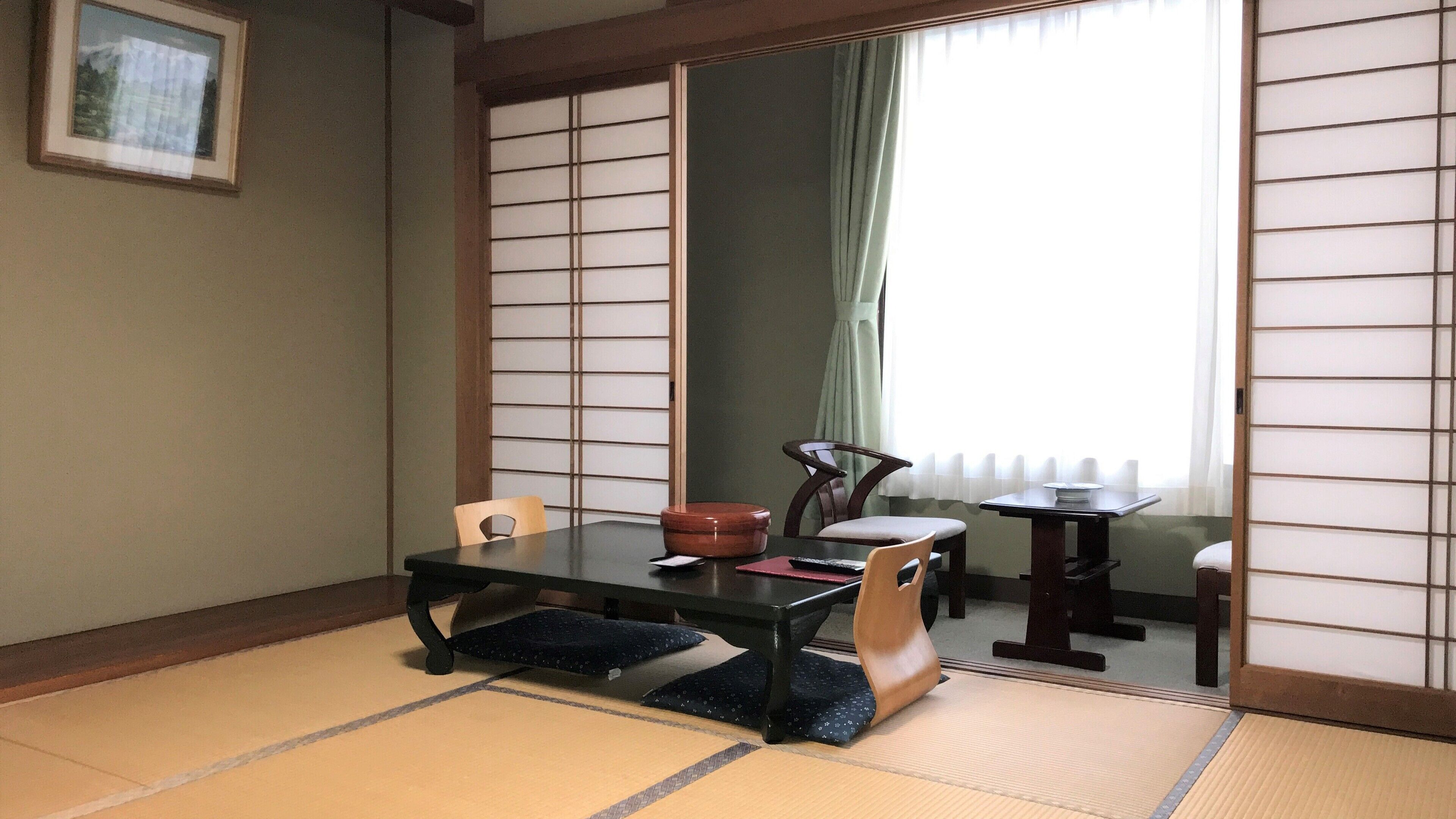 Una habitación japonesa tradicional con suelo de tatami, una mesa baja, sillas y un panel corredizo shoji.
