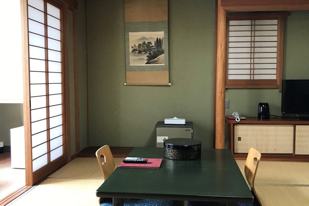 Una habitación japonesa tradicional con suelo de tatami, una mesa baja, un televisor y un armario.