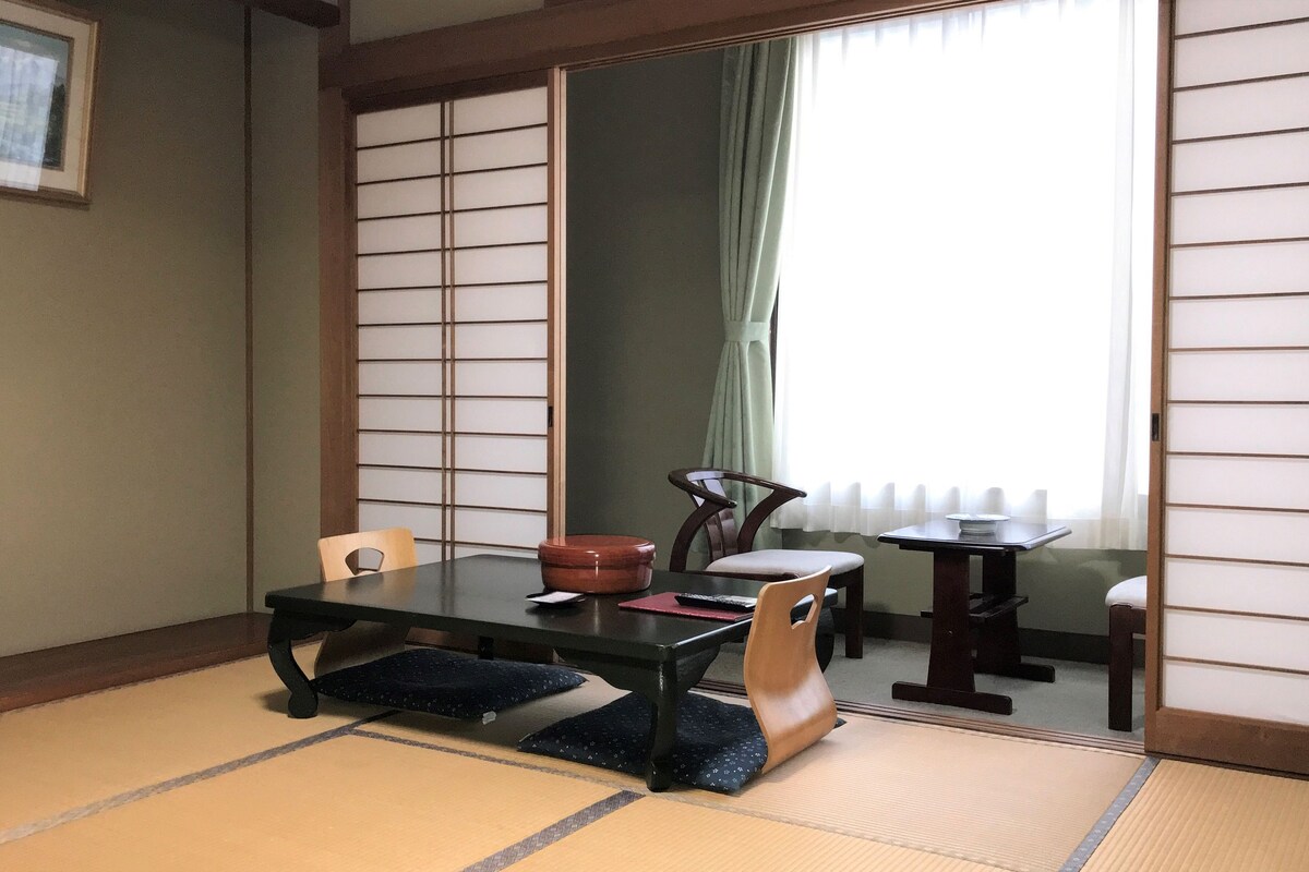 Een traditionele Japanse kamer met tatami vloerbedekking, een lage tafel, stoelen en een verschuifbare shoji-scherm.