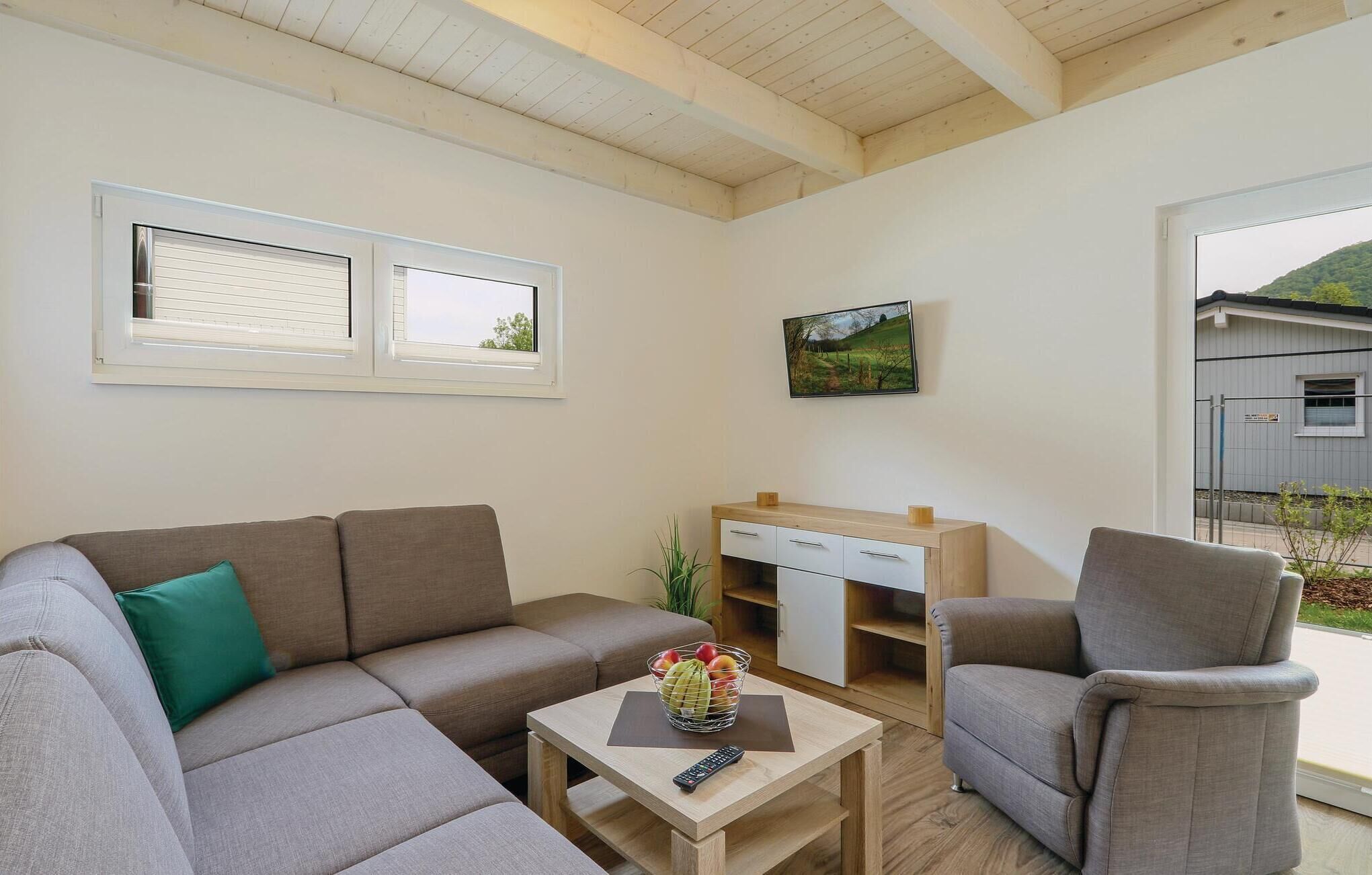 A living room with a sofa, a chair, a small table with a basket of fruit, a remote control, and a painting on the wall.