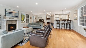 A spacious living room with a fireplace, a dining area, and a kitchen with bar stools. - Luxury Home a Short Walk to Beach and Town with Amazing Reviews  (Point Pleasant Beach)