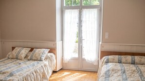 A room with two beds, a wooden floor, and a door with curtains.