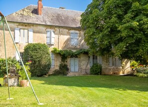 A two-story stone house with a well-maintained lawn, a large tree, and a visible front door. - Homerez - Apartment in Rouffilhac (Rouffilhac)
