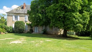 A stone house with a well-maintained lawn, a large tree, and a clear sky.
