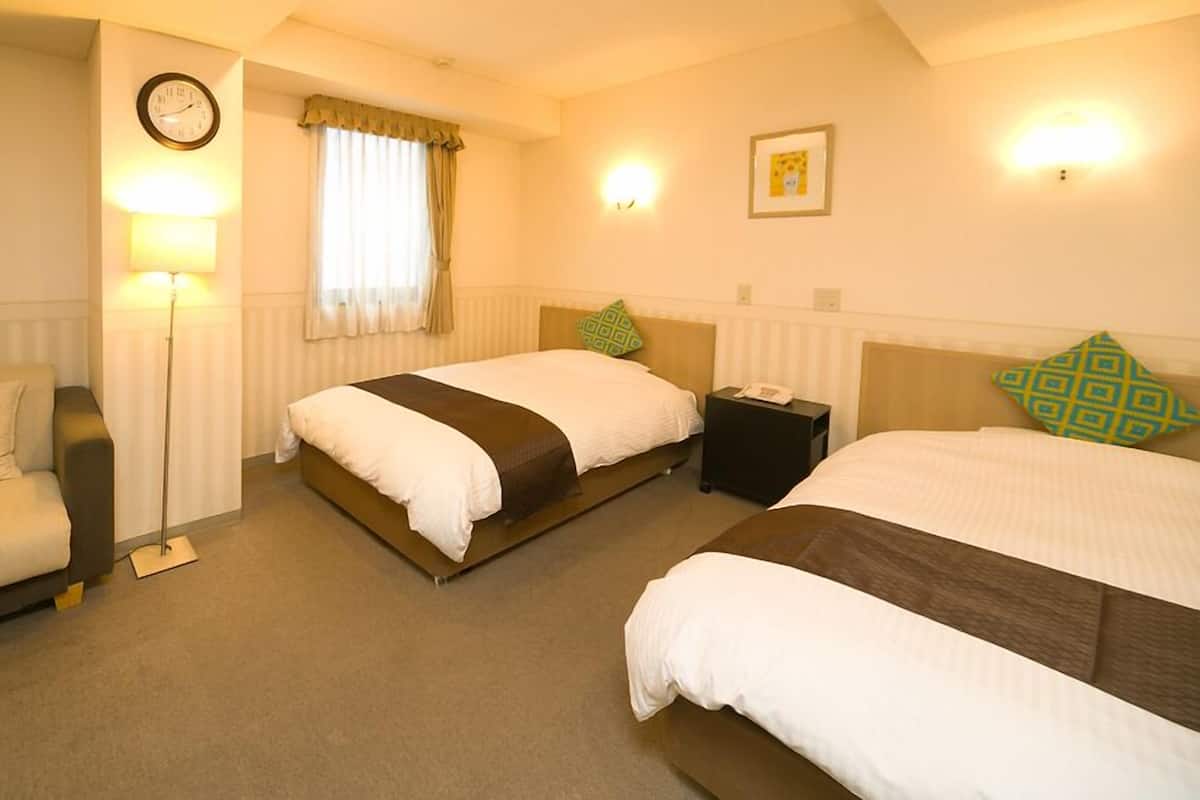 A hotel room with two beds, a sofa, a bedside table with a phone, a lamp, a clock, and a window with curtains.