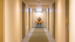 A hotel hallway with a carpeted floor, a reception desk with a flower arrangement, and a sign above the desk.