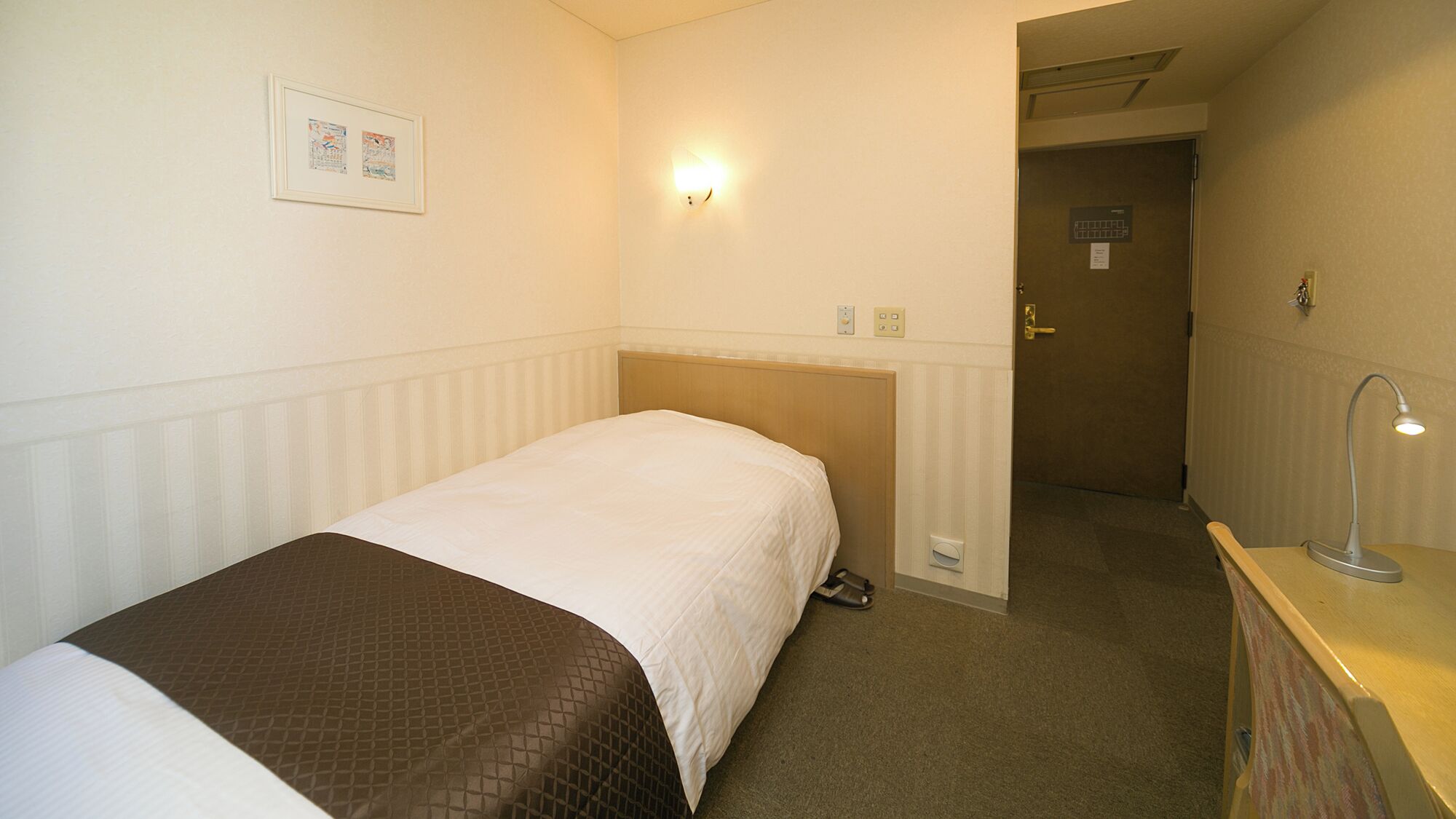 Habitació d'hotel amb llit, escriptori amb làmpada, porta i llum penjada a la paret.