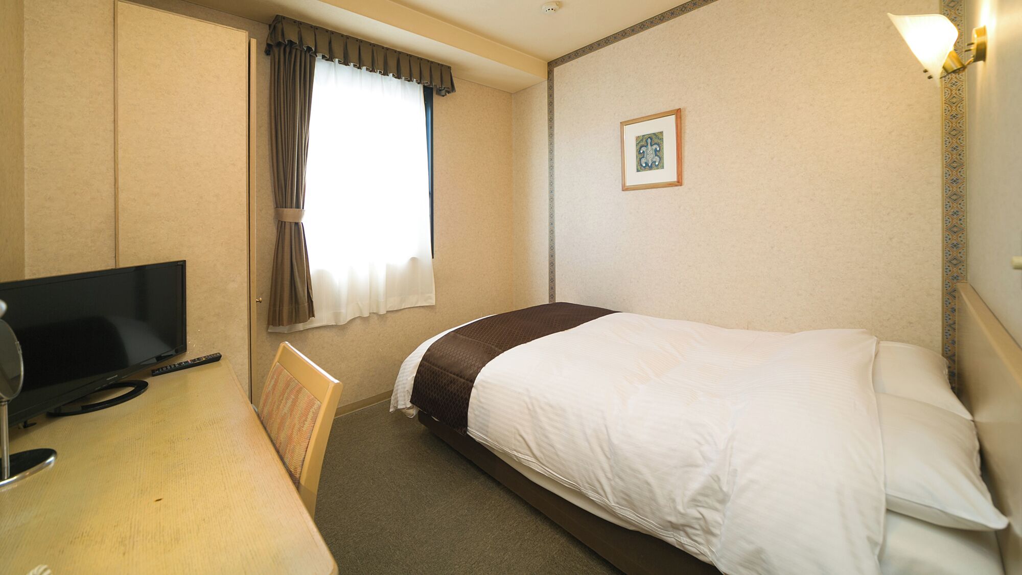 Habitació d'hotel amb un llit, escriptori amb televisió, cadira, finestra amb cortines i un quadre penjat a la paret.