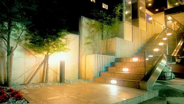 Un edificio moderno con una escalera, iluminación exterior y un árbol.