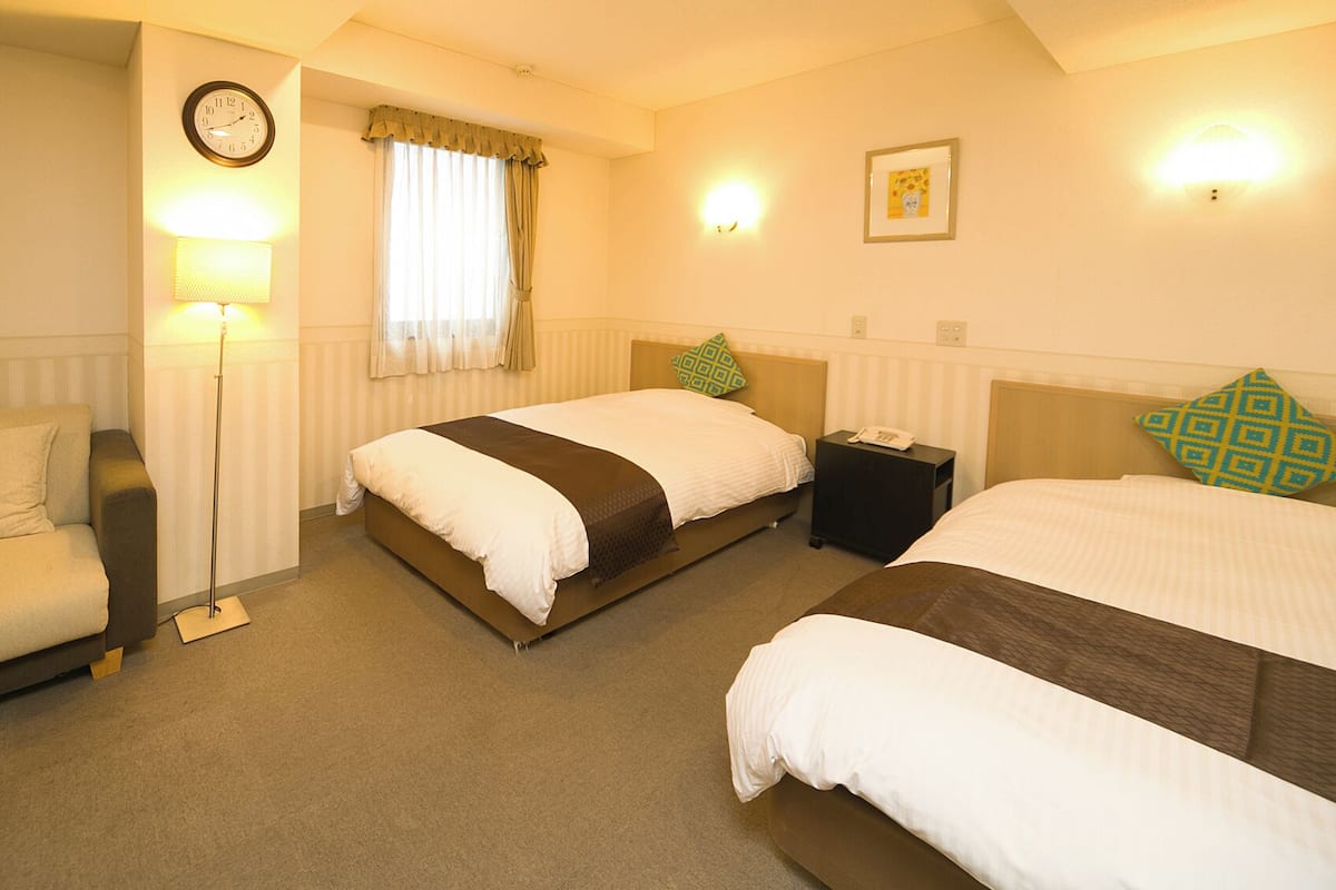 A hotel room with two beds, a sofa, a lamp, a clock, and a framed picture on the wall.