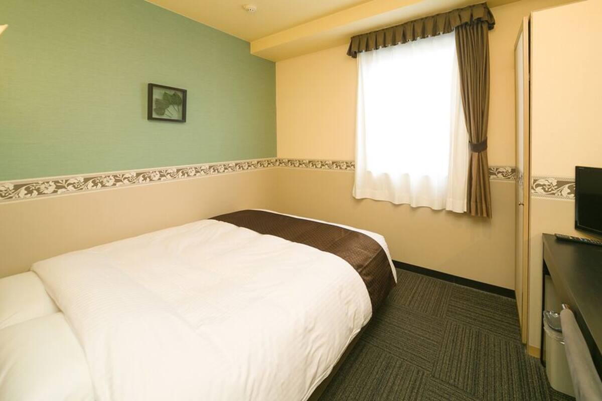 A hotel room with a bed, a television, a window with curtains, and a wall-mounted picture.
