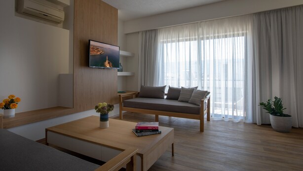 A modern living room with a sofa, a coffee table, and a TV mounted on the wall. - Lissou Apartment (Chania)
