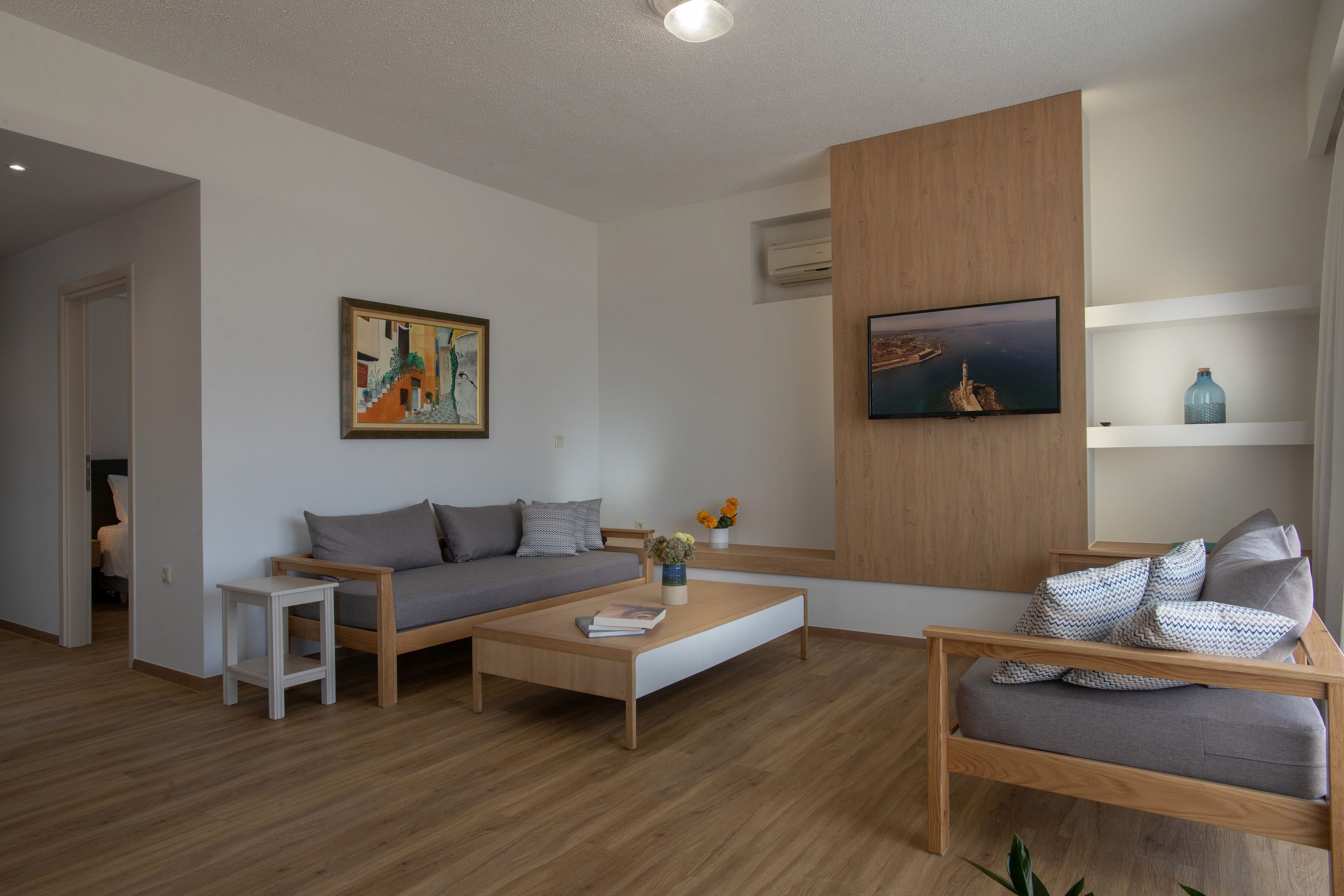 A modern living room with a sofa, coffee table, and TV. There is a painting on the wall and a small table with a vase of flowers.