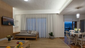 A modern living room with a sofa, a dining table with chairs, a TV mounted on the wall, and a large window with curtains. - Lissou Apartment (Chania)