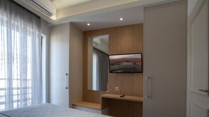 A bedroom with a bed, a TV mounted on a wooden panel, a window with curtains, and a door. - Lissou Apartment (Chania)
