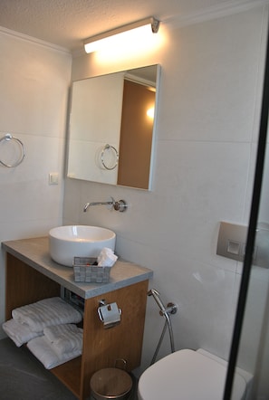 A bathroom with a white sink, mirror, and shower. There are towels and a soap dish on the counter. - Lissou Apartment (Chania)