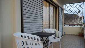 A balcony with two white chairs and a small table, a sliding glass door, and a view of the neighborhood. - Lissou Apartment (Chania)