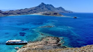 A coastal landscape with a large ship docked near rocky shores, surrounded by clear blue waters and a prominent mountain in the background. - Lissou Apartment (Chania)
