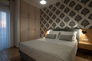 A bedroom with a bed, wooden headboard, patterned wallpaper, and a nightstand with a lamp. - Poli Apartment (Chania)