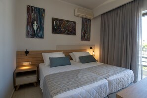 Une chambre à coucher moderne avec une tête de lit en bois, deux tableaux, une table de chevet et une grande fenêtre avec des rideaux.