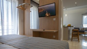 A modern hotel room with a large bed, a mounted TV, and a view of a coastal landscape. - Poli Apartment (Chania)