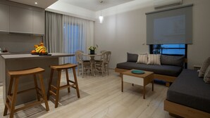 A modern living room with a sofa, wooden stools, a coffee table, and a dining area with a table and chairs. - Poli Apartment (Chania)