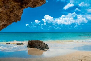 Une plage à l’eau turquoise et limpide, un rivage sablonneux et une grande formation rocheuse au premier plan.