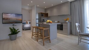 A modern kitchen with a central island, wooden stools, a flat-screen TV, and a potted plant. - Poli Apartment (Chania)
