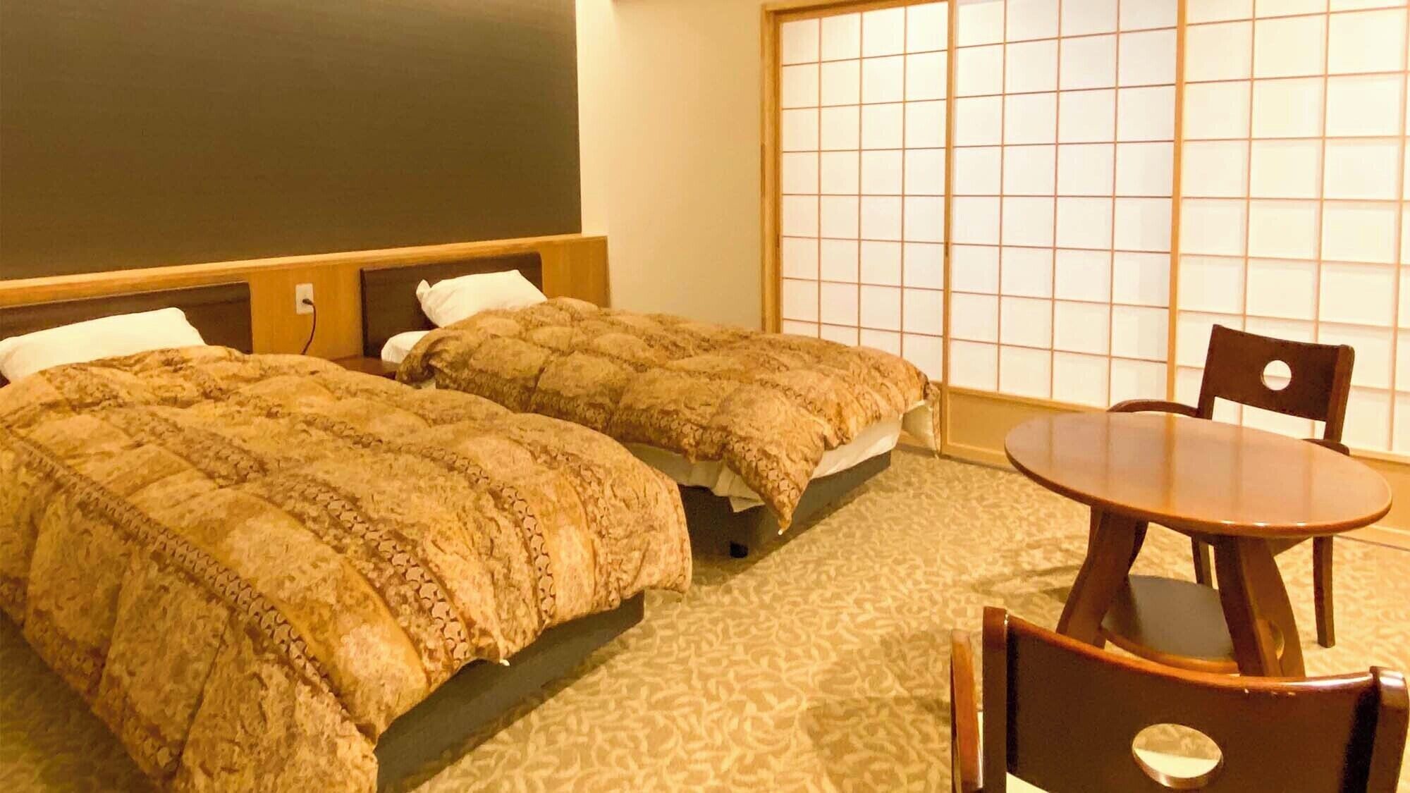 A hotel room with two beds, a wooden headboard, a tatami mat wall, a round wooden table, and a chair.